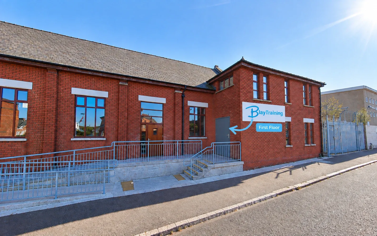 The Blay Training building at 4 Nubia St, Belfast: red-brick building with the Blay Training sign; an arrow points to the grey door on the right, marked First Floor.
